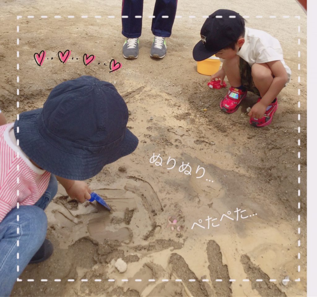 雨上がりの滑り台下の土で泥んこ遊びをしている園児たち