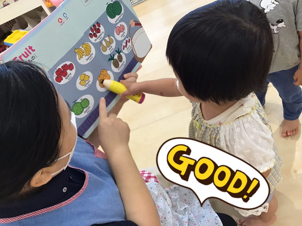 ペンを持って絵本の食べ物を指す園児