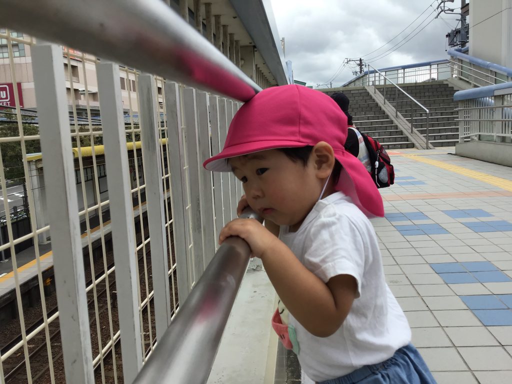 手すりの隙間から線路を見つめる園児