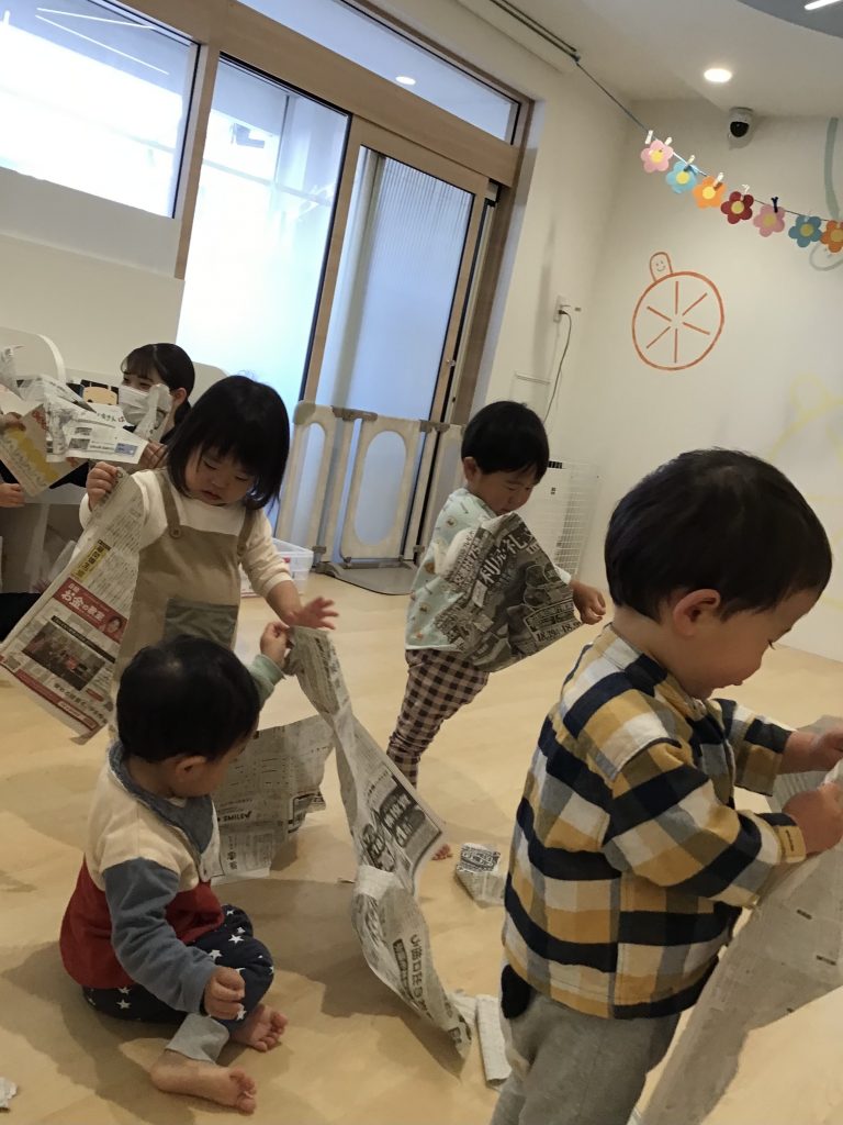 一枚の新聞紙を破いたり自由に遊ぶ園児たち