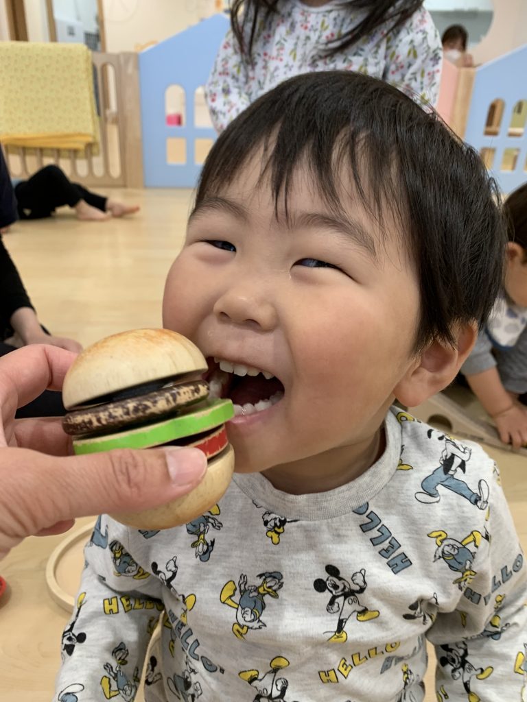 おもちゃのハンバーガーを食べようとする園児