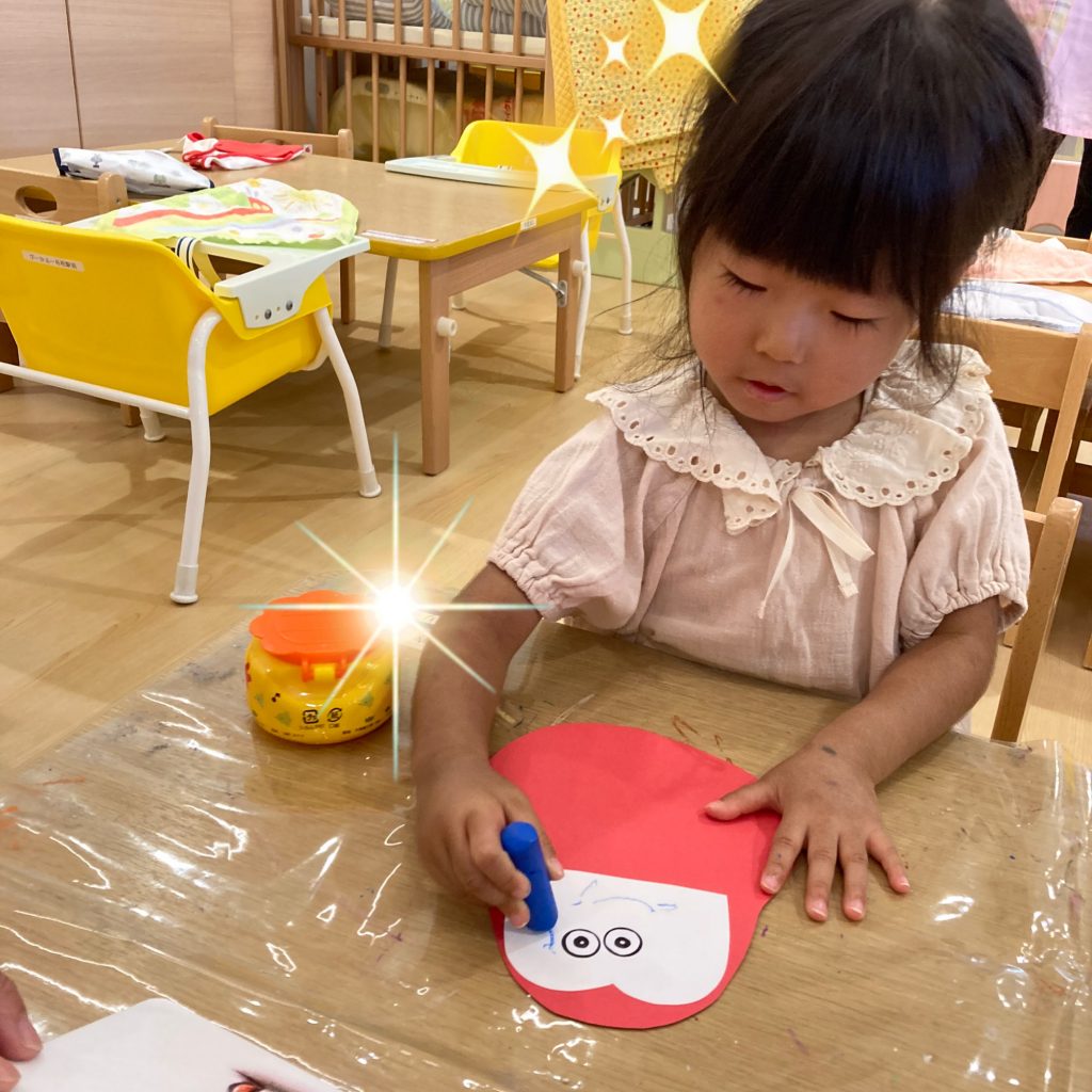 だるまさん方の顔にクレヨンで絵を書く園児