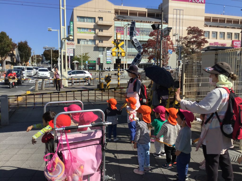 お散歩中踏切で電車を見ている園児たち