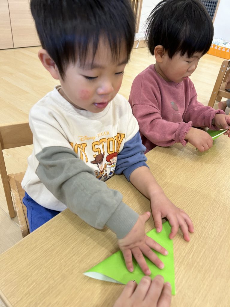 黄緑の折り紙を三角に折る園児