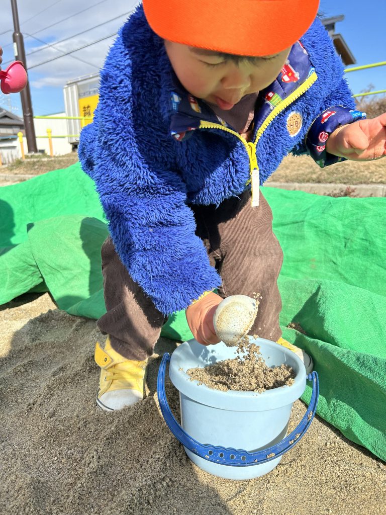 バケツに砂を入れる園児