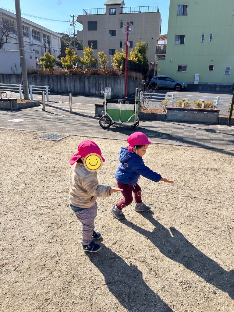 公園で片手を出してシャボン玉を触ろうとする園児たち