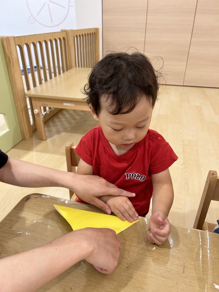 黄色い折り紙を三角に折る園児